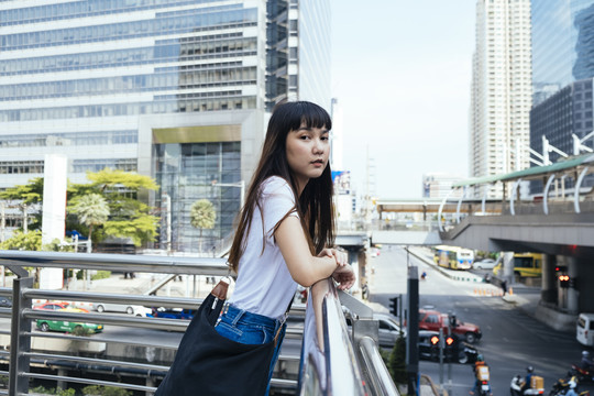 在城市里，一个可爱的亚洲时髦女人靠在扶手上。曼谷年轻女旅行者的时尚肖像。