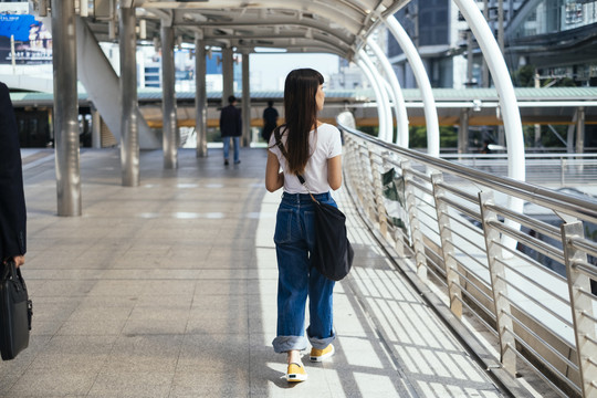 穿着白色衬衫和蓝色牛仔裤的可爱的亚洲女人在城市的人行道上摇摇欲坠