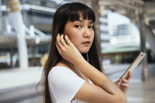 一位留着刘海发型的可爱亚洲年轻女子手持智能手机看着相机。