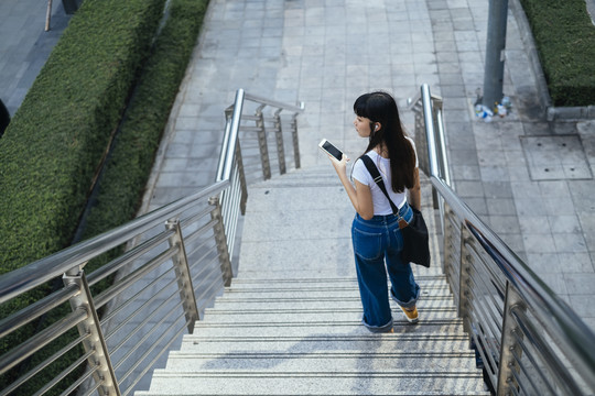 在城市里，一位年轻的时髦女人拿着智能手机走下楼梯。