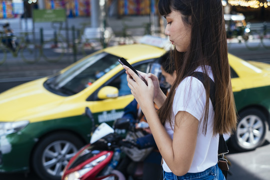 一名亚裔泰国妇女用智能手机打电话给出租车服务来接她。
