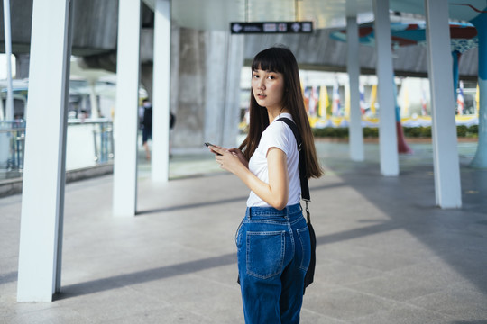 可爱的泰国女孩在城市人行道上行走时使用智能手机。