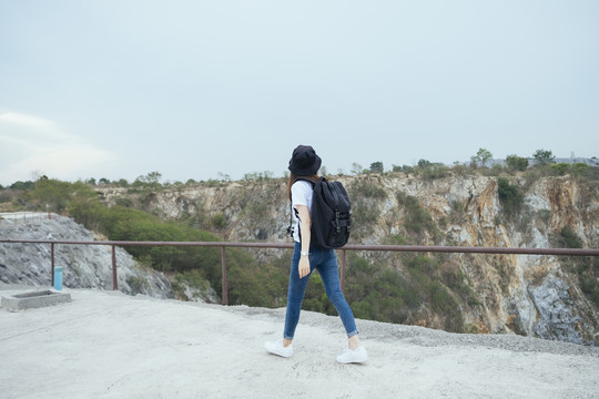 侧视图-年轻的亚泰黑头发旅行家妇女戴着帽子在山区户外散步。