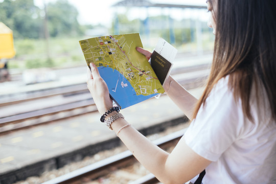 在火车站，一位年轻的亚裔泰国长毛黑发女旅行者正在看地图和泰国护照。