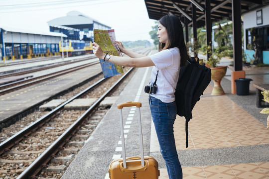 在火车站，一位年轻的亚裔泰国长毛黑发女旅行者正在看地图和泰国护照。