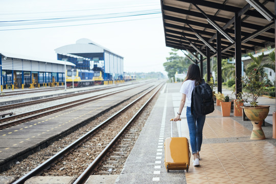 一位年轻的亚裔泰国长黑发女旅客在车站月台等火车。