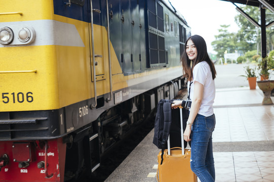 年轻的亚裔泰国长毛黑头发女旅行者在火车站站台等火车。