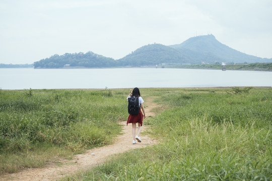 后视图-年轻的亚泰黑头发旅行家女子走进湖中。