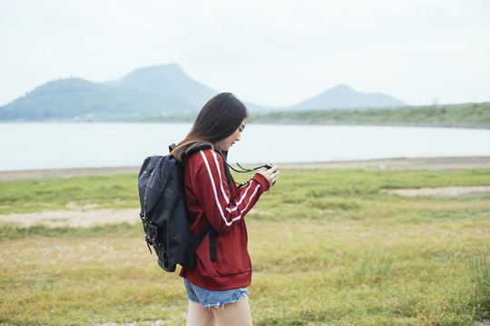 在春武里湖边，一位年轻的亚裔泰国长发旅游妇女手持相机。
