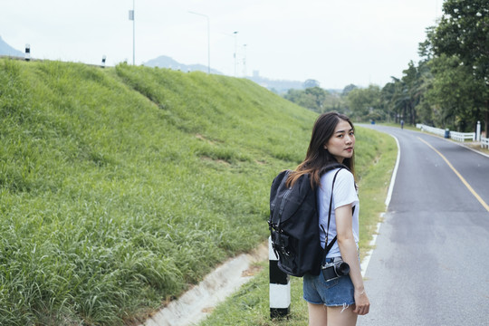 年轻的亚裔泰国长毛黑发女旅行者在路上搭便车。