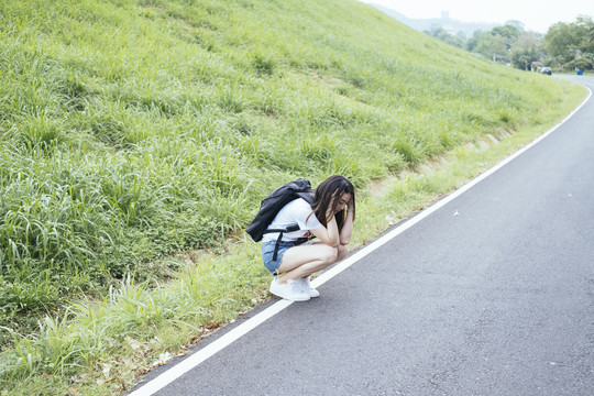 年轻的亚裔泰国长黑发女旅行者在路上等车。搭便车的人。