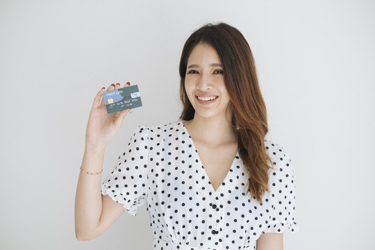 身穿黑白圆点连衣裙的快乐泰国年轻女子，在白色背景下展示信用卡。