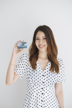 身穿黑白圆点连衣裙的快乐泰国年轻女子，在白色背景下展示信用卡。