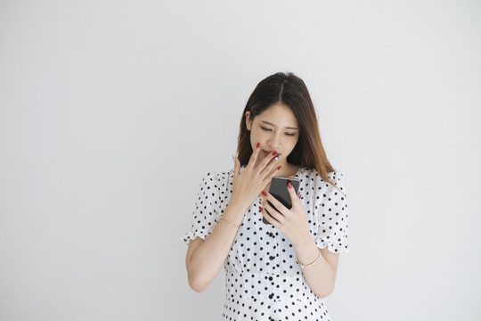 穿着黑白圆点连衣裙的开朗女人在智能手机上看到促销活动时感到惊讶。在白色背景上隔离。