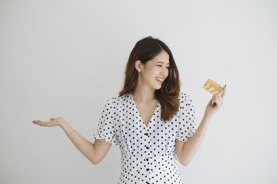 身穿白色连衣裙和黑点的亚洲女性，左手持信用卡，右手空着，以便在信用卡上放置任何产品。隔离在白色背景中