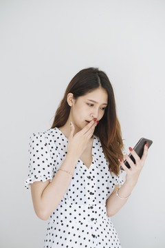 一位穿着黑白圆点连衣裙的年轻泰国女士手持智能手机，看着手机上的购物促销。在白色背景上隔离。