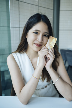 微笑的亚洲女人坐在咖啡馆里，幸福地拿着信用卡的特写镜头。