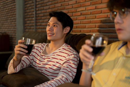 一对亚洲LGBTQ+男性喜欢在家里一起喝酒和看电视。