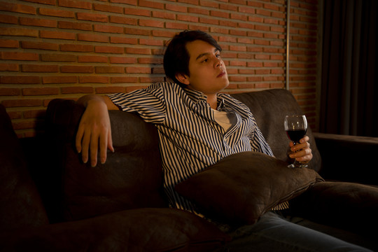 亚洲年轻人独自在沙发上喝酒，晚上看电视。