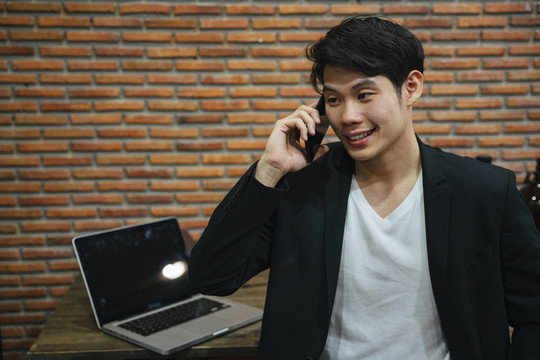 亚洲年轻商人在砖砌办公室打电话。