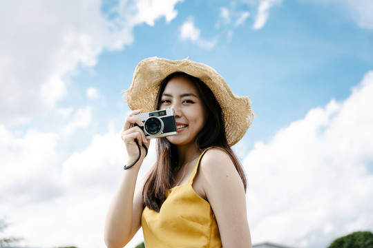 美丽的亚洲女旅行者在明亮的天空背景下用复古胶卷相机拍照。