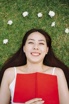 俯视图-躺在草地上的美丽亚洲旅行家妇女的画像，带着红皮书。