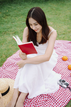 穿着白色连衣裙的美丽亚洲女人在公园户外看书。