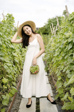 美丽的亚洲农妇在当地农场戴着带菜篮的帽子。