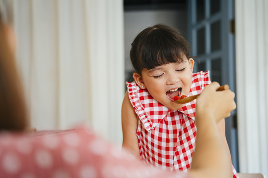 亚洲小孩用母亲的勺子吃食物。