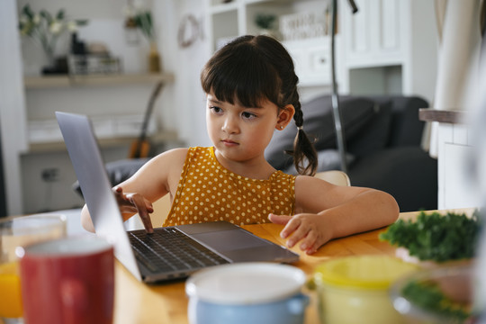 亚洲小女孩在笔记本电脑上做作业，并请妈妈帮助她。