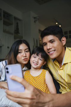 亚洲家庭在家里用智能手机拍摄自拍照片。