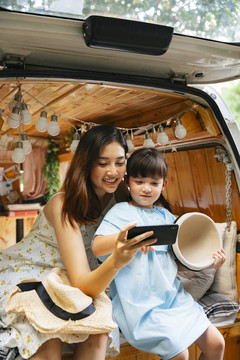 亚洲母亲和孩子在房车行李箱用智能手机自拍，玩得很开心。