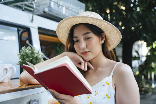 美丽的亚洲女人戴着帽子在花园里看书的肖像。