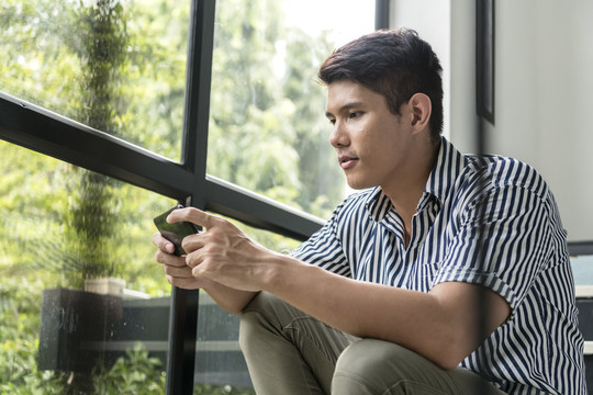坐在楼梯上用智能手机玩手机游戏的亚洲男人的肖像，表情严肃。