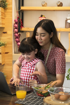 亚洲家庭的母亲和女儿在家里的厨房里一起做饭。他们都在网上寻找食物配方。