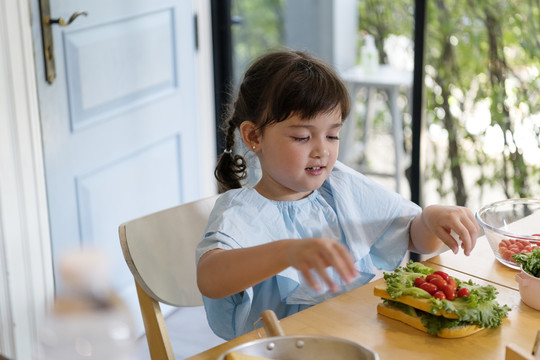快乐的亚洲孩子喜欢在家吃蔬菜三明治当早餐。