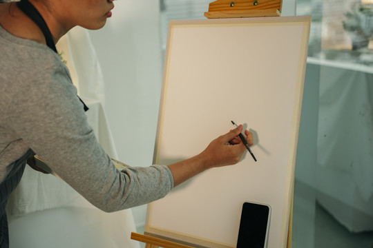 后视图-专业女艺术家在画布上使用毛笔绘画。画架模型。