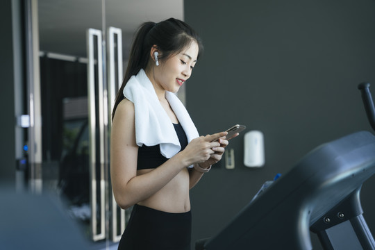 健康的亚洲女性在跑步机上锻炼时在智能手机上选择流媒体歌曲。