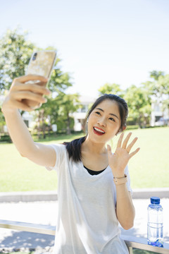 运动型亚洲女性在公园里用智能手机闲聊锻炼或自拍。