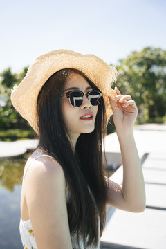 在游泳池附近，一位美丽的亚洲旅行者戴着太阳镜和帽子。