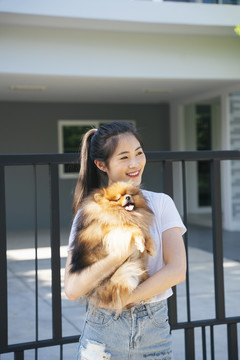 美丽的亚洲女人和她的狗站在房子的前门。