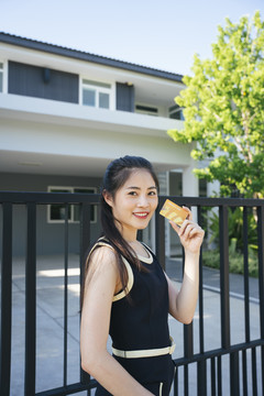 美丽的亚洲女人在豪宅前用信用卡。购买地产的概念。