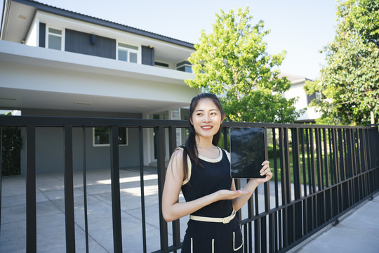 一名亚洲妇女在屋前展示数码笔记本电脑。投资理念。