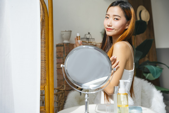 看着镜子，美丽的年轻亚洲女人用化妆品化妆。