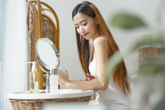 侧视图-亚洲女性在家里用乳液霜护肤手臂。