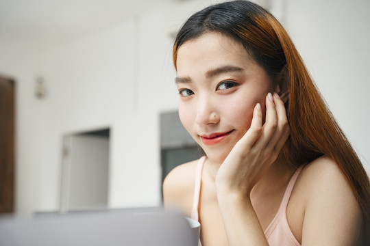 在家里用笔记本电脑工作的年轻亚洲女性的特写照片。