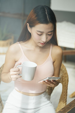 一位年轻漂亮的亚洲女性手持智能手机，端着一杯咖啡的照片。