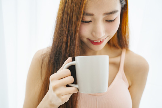 在白色背景上，一位年轻的亚洲女性拿着一杯咖啡的特写镜头。