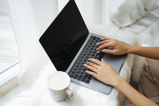 一名自由职业妇女在白色毛皮桌子上用笔记本电脑工作。