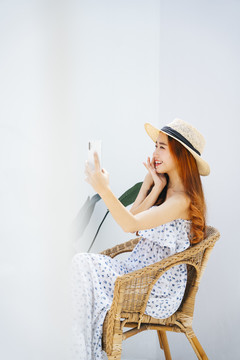 侧视图-美丽的亚洲女旅行者戴着帽子，在椅子上使用智能手机。